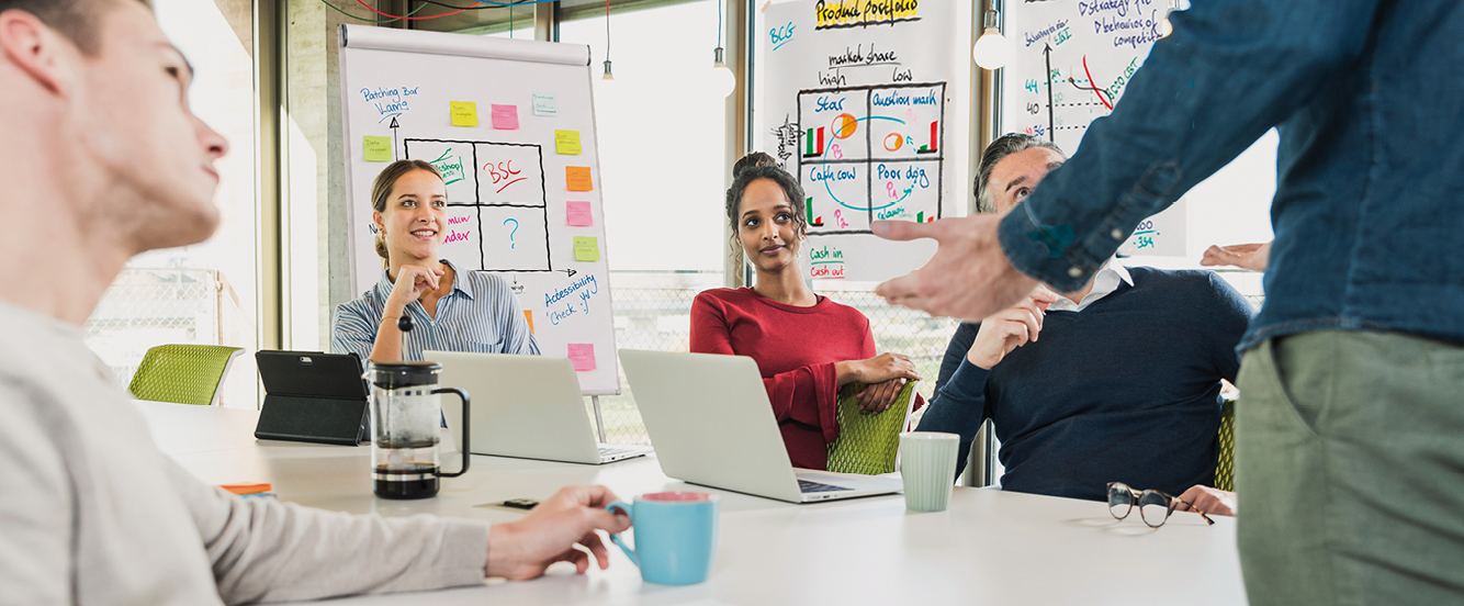 Teilnehmende eines Inhouse-Trainings der CA controller akademie diskutieren gemeinsam in einem Meetingraum mit Whiteboards und Laptops.